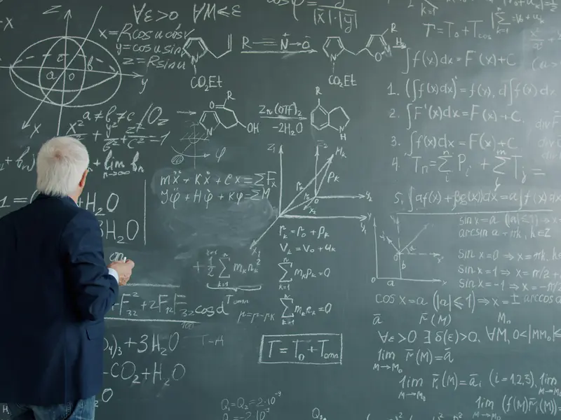 A teacher writing on a chalkboard covered edge to edge in equations