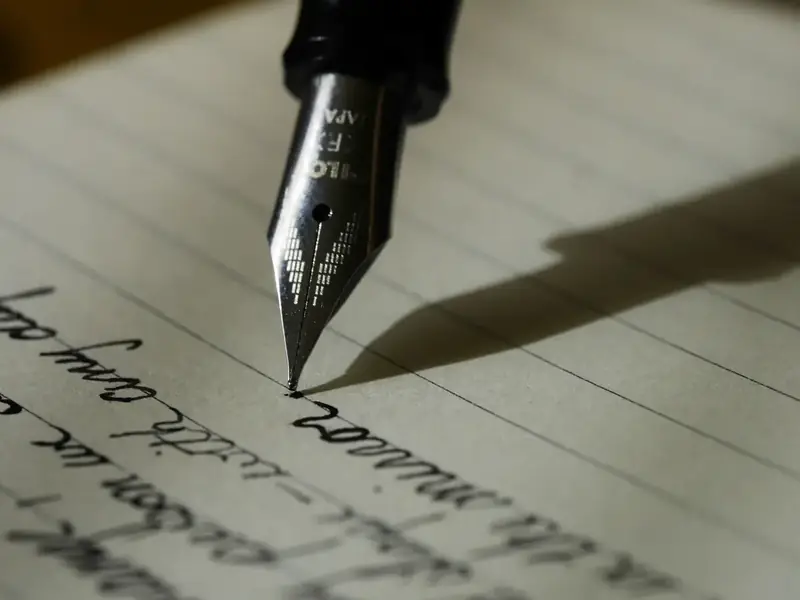 A fountain pen nib writing in cursive on lined paper