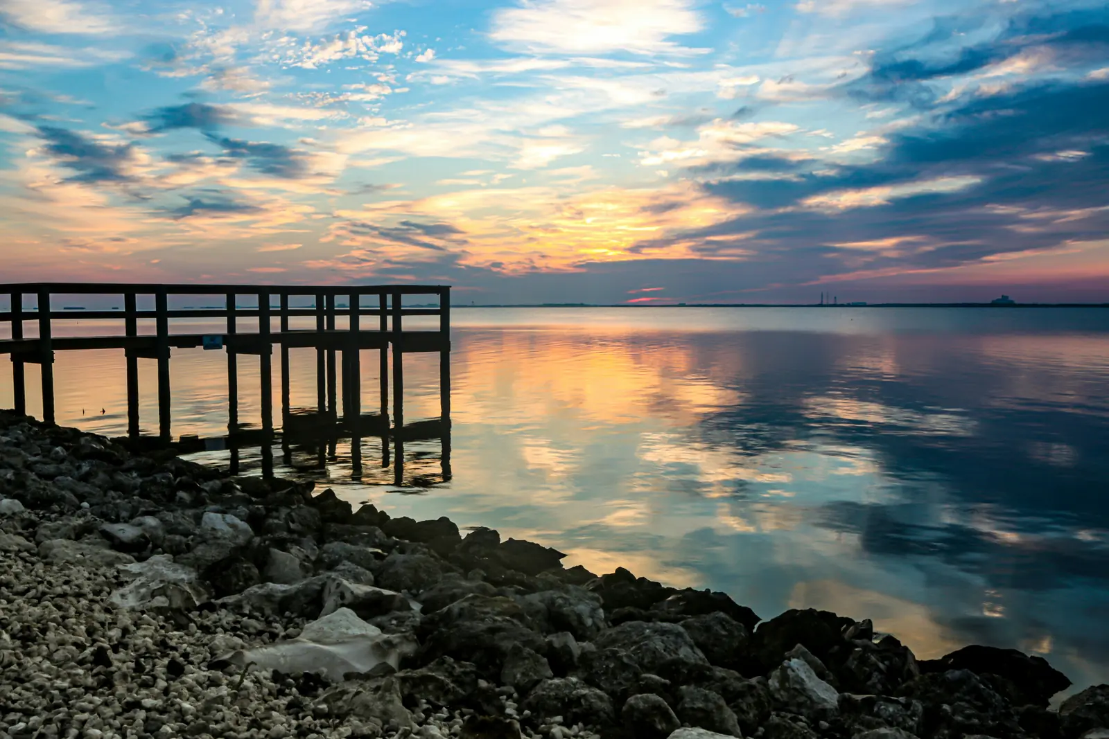 A wooden pier reaching into calm water under a sunrise sky