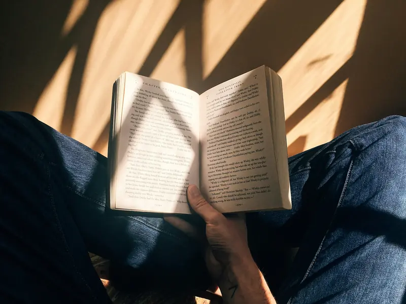 An open paperback held in a reader&rsquo;s lap in warm afternoon light
